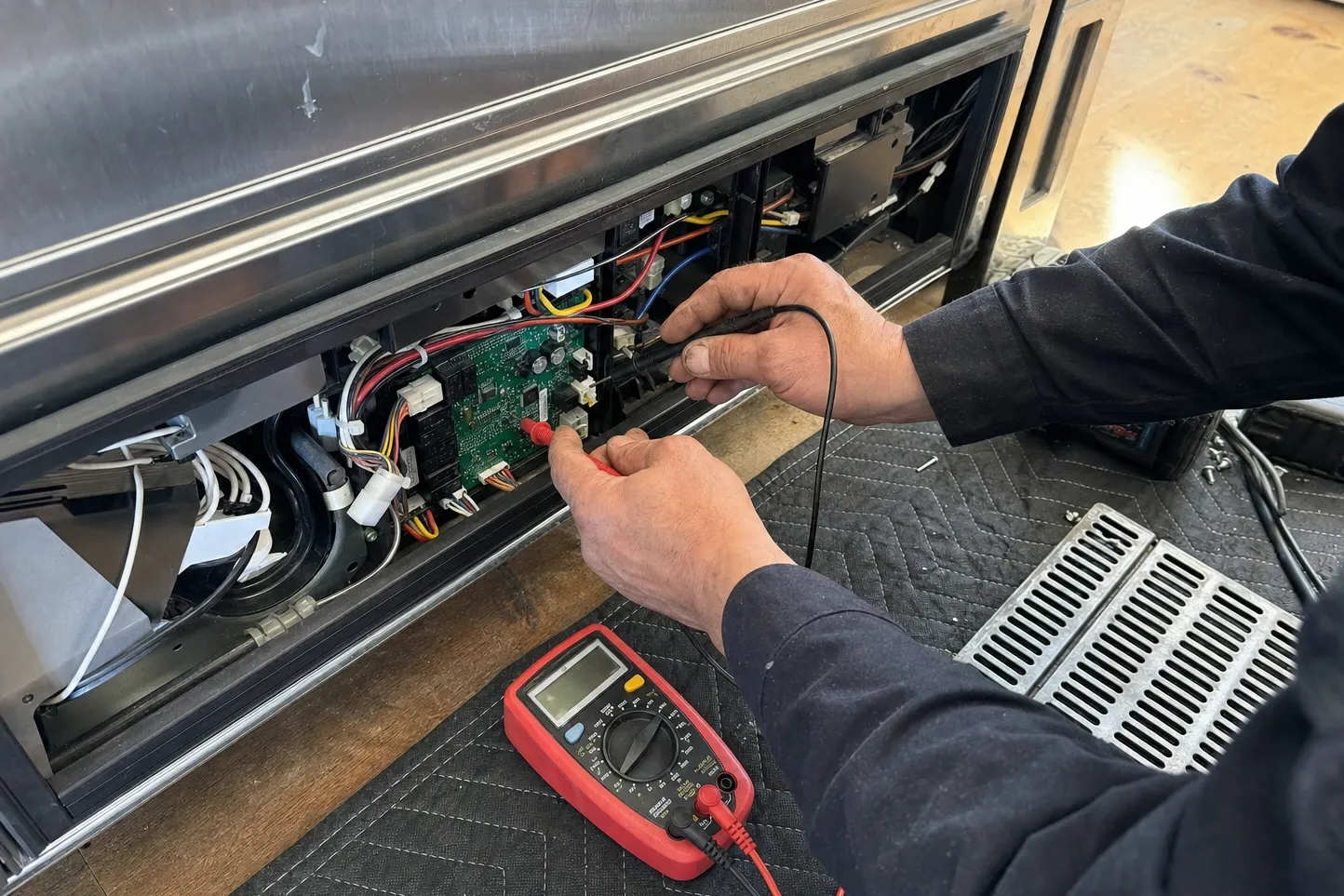 Meter probes on the green main control board behind the removed lower panel of a built-in cabinet