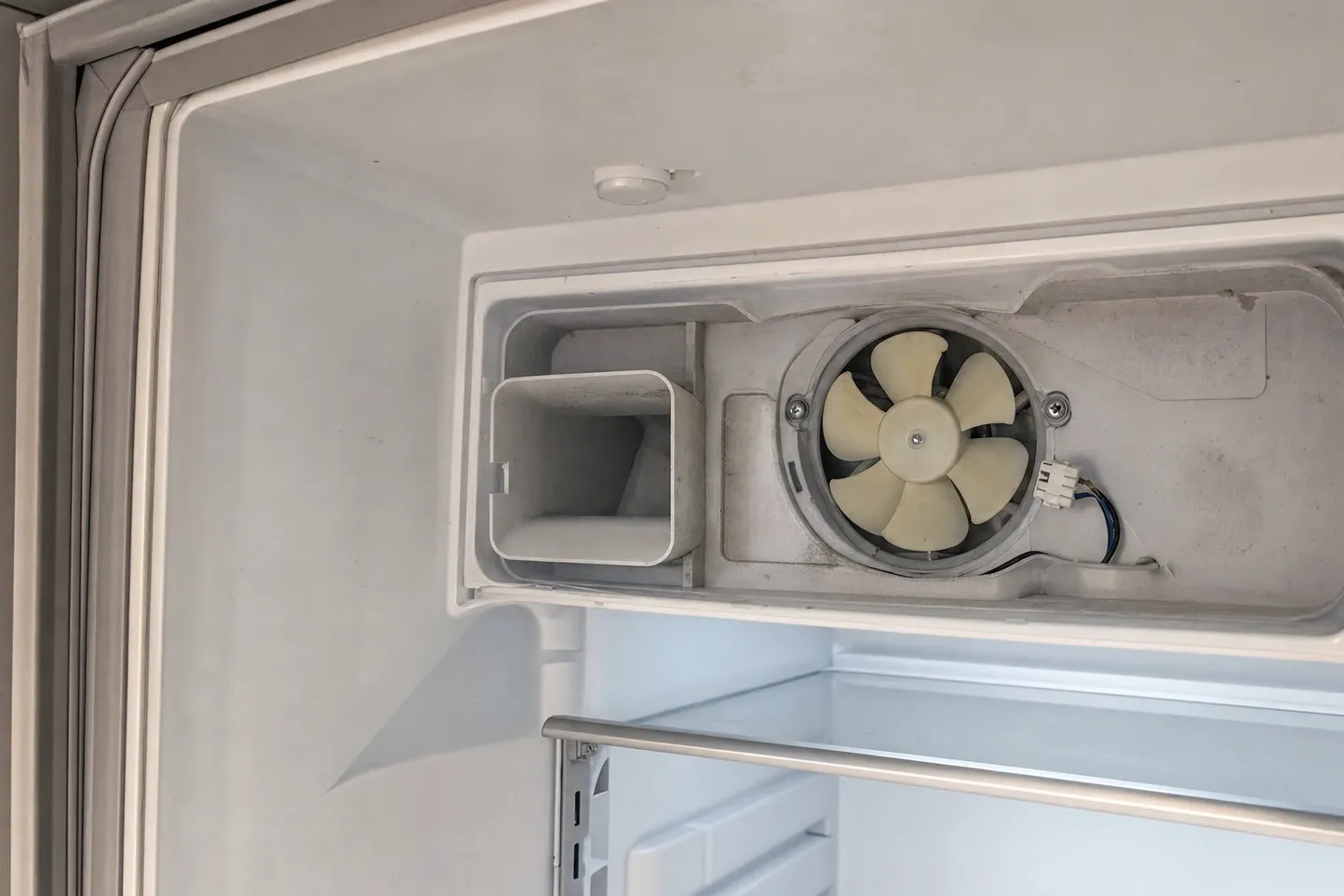 Duct cover lifted inside a fresh-food compartment, exposing the pale evaporator fan, the cold-air duct and the ceiling light